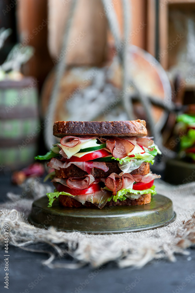 Big sandwich with bread, prosciutto, lettuce, tomtatoes, cucumber and cheese in the kitchen