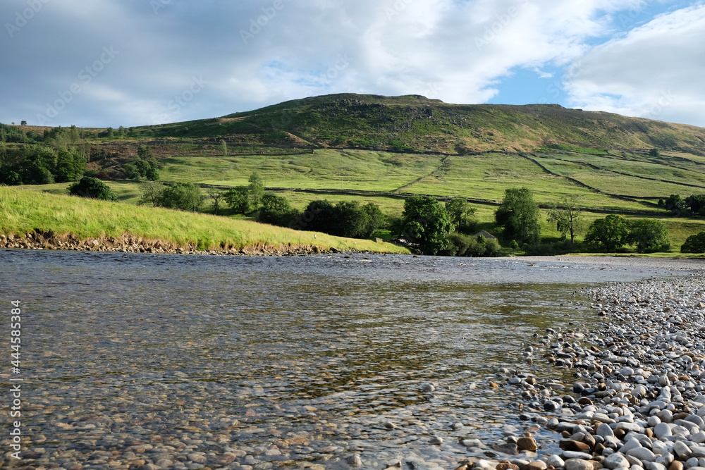 Fototapeta premium A view looking south along the River Wharfe toward Burnsall and Thorpe Fell, in the Yorkshire Dales, North Yorkshire.