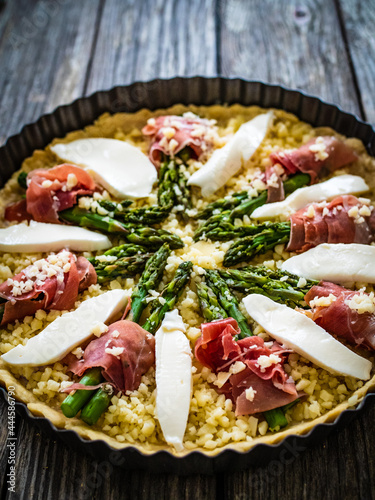 Uncooked tart with asparagus and serrano ham on wooden table 