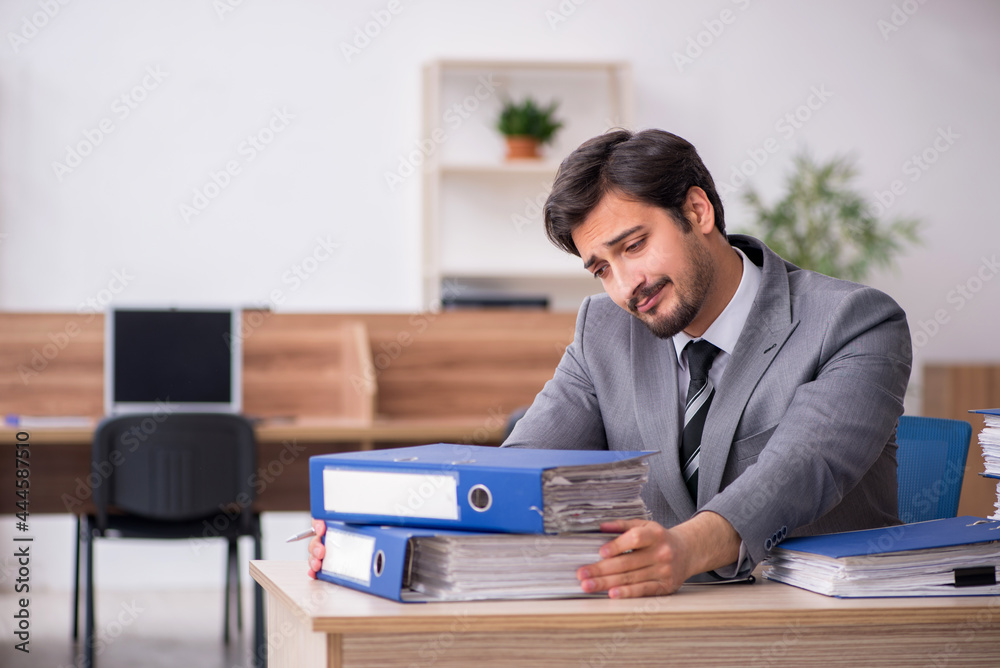 Young male employee unhappy with excessive work in the office Young male employee unhappy with excessive work in the office