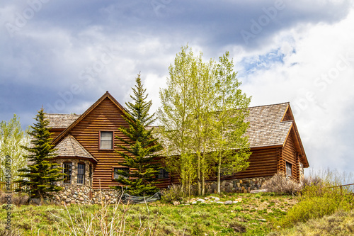 Luxury log cabin with wooden roof and rock bay window on hilltop surrounded by pines and quaking aspens