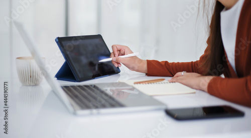 Focus on hand young asian woman holding stylus pen pointing on digital tablet while she working at home with computer laptop