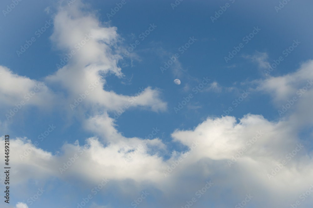 Blue sky evening with clouds rolling in. Moon peeking through the clouds.