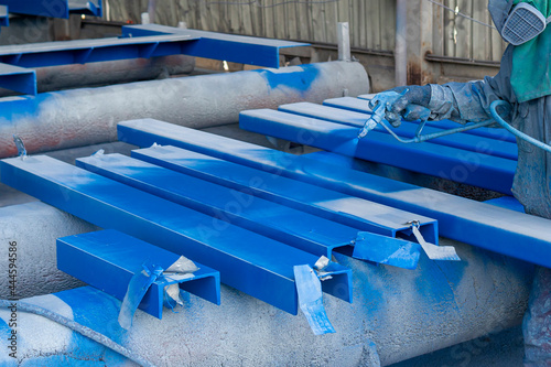 Painter is working to painting color top coat on steel structure with spray gun, at industrial factory.