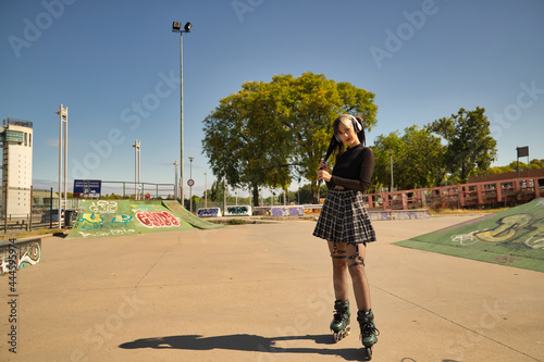Cute young girl with heterochromia and punk style with white headphones and inline skates holding her pigtails with one hand looking at the camera.