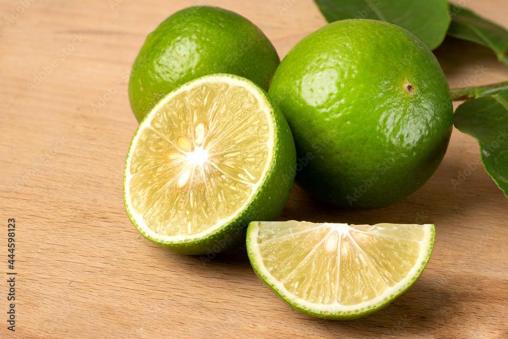Close up natural fresh lime with sliced, green leaf, on wooden table.