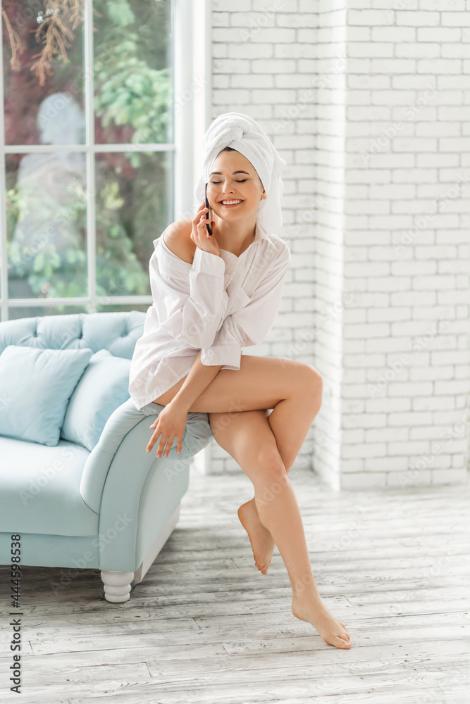 Pretty woman wrapped in a shower towel using mobile phone while sitting on bed