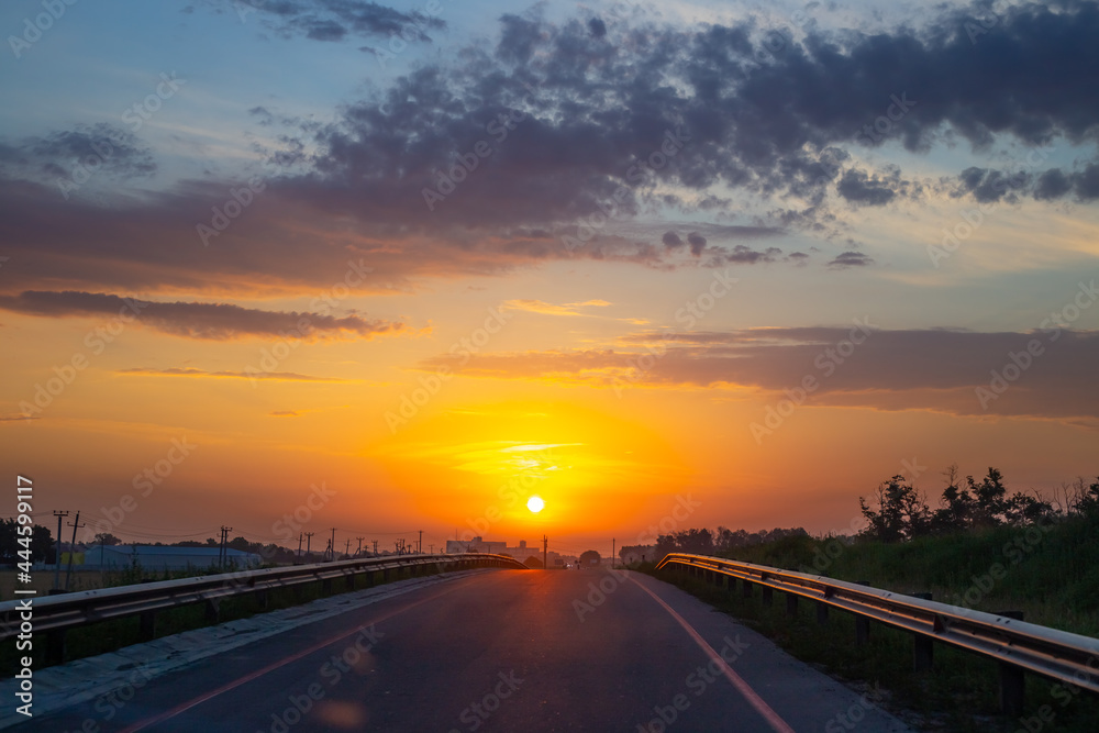 Dawn on the road. The bright sun rises against the orange sky. Morning landscape