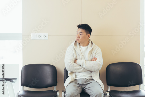 young asian man waiting for an interview or meeting sitting in the hallway in the waiting room. Student or entrant in the reception for exam or employment hr. Male patient in office a hospital clinic