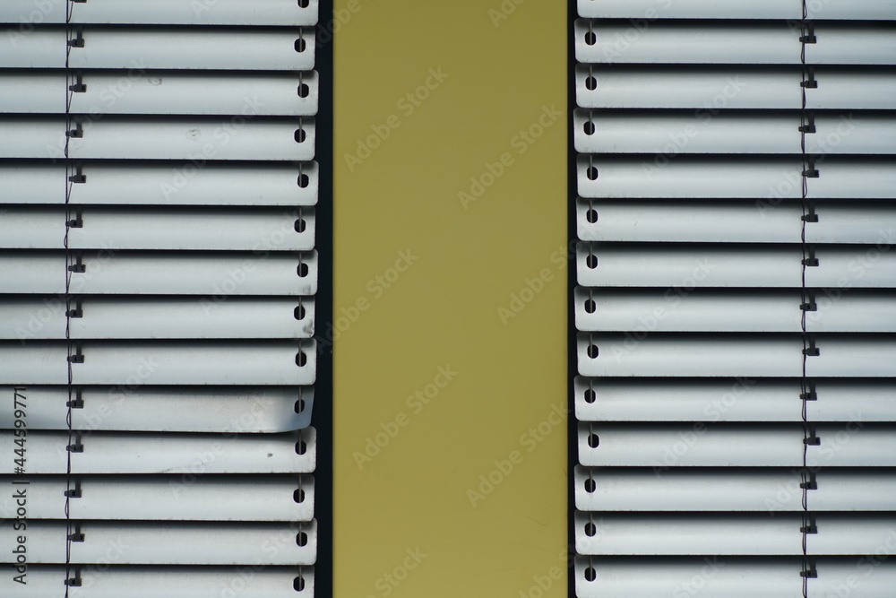 Architektur im Detail mit einem Sonnenschutz aus Aluminium Jalousien in grau und hellgelben Flächen aus Metall