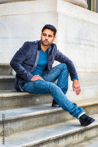 Obraz na płótnie Dressing in a dark purple woolen blazer, blue jeans and black leather shoes, a young handsome Middle Eastern man is sitting on steps outside an office, thoughtfully looking around.. w salonie
