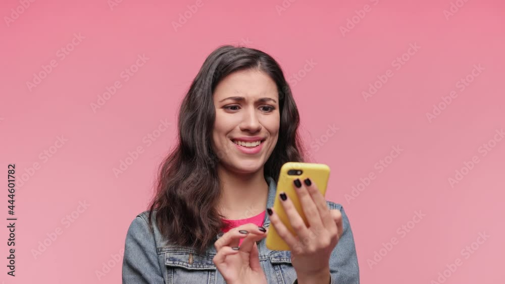 Shocked smiling happy beautiful girl 20s years in casual jacket pink t-shirt posing isolated on pink background in studio. People lifestyle concept. Look surprised wow hold using mobile cell phone. Shocked smiling happy beautiful girl 20s years in casual jacket pink t-shirt posing isolated on pink background in studio. People lifestyle concept. Look surprised wow hold using mobile cell phone.