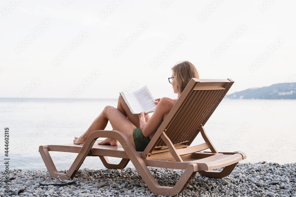 The beautiful young woman sitting on the sun lounger reading a book