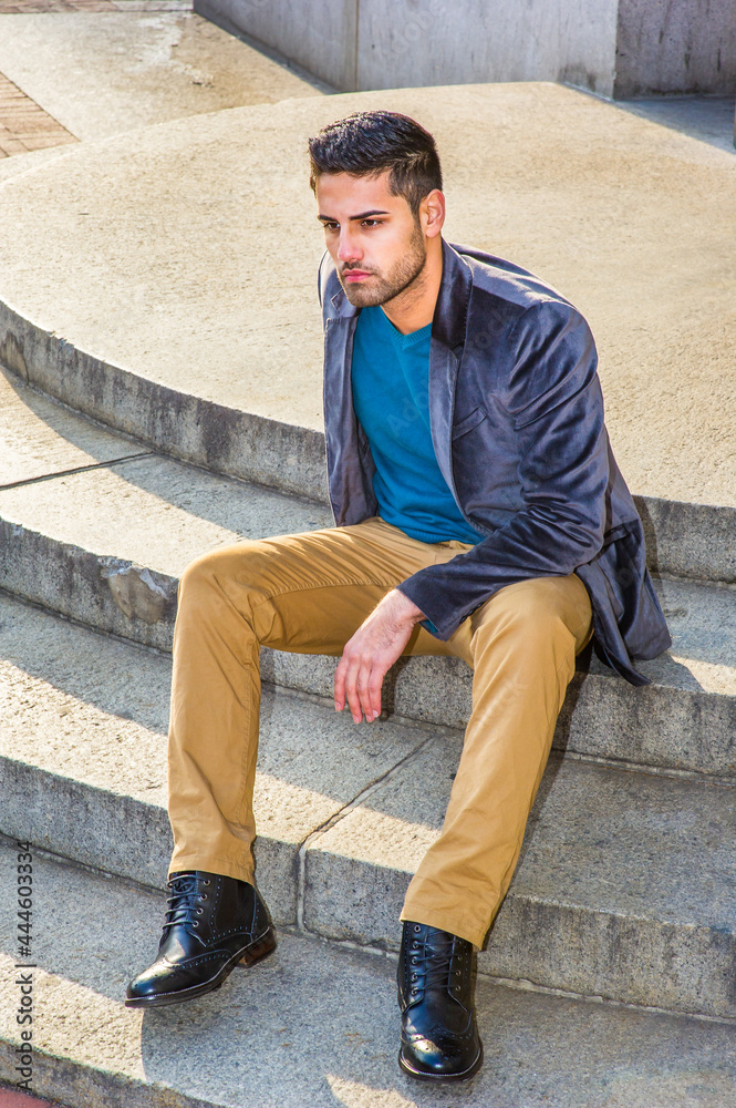 Dressing in a dark purple woolen blazer, dark yellow pants and leather boot shoes, a young Middle East guy with bread and mustache is sitting on circle steps, relaxing and thinking. Dressing in a dark purple woolen blazer, dark yellow pants and leather boot shoes, a young Middle East guy with bread and mustache is sitting on circle steps, relaxing and thinking.