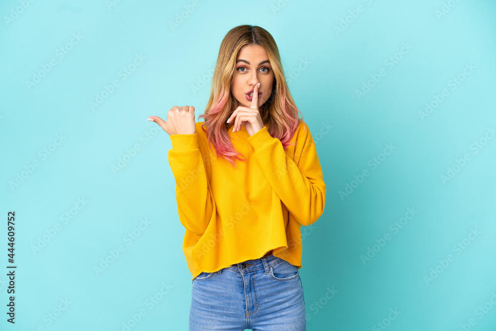Young woman over isolated blue background pointing to the side and doing silence gesture