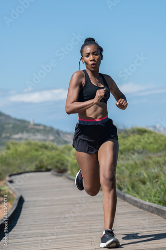 Fototapeta Naklejka Na Ścianę i Meble -  Afro american woman running fast along a wooden runway: Exercise concept.
