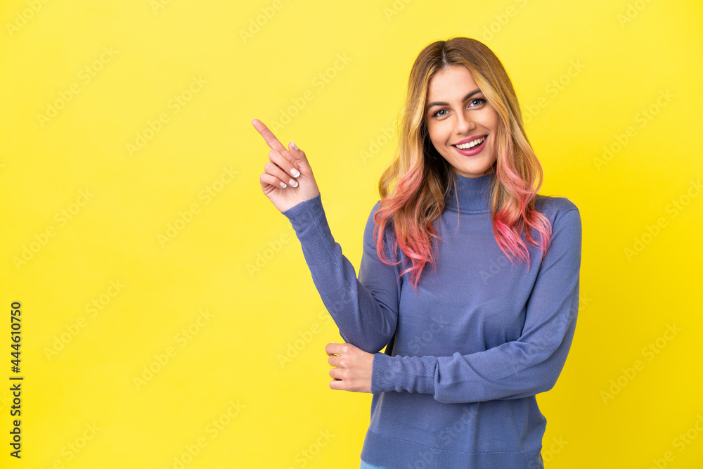Young woman over isolated yellow background happy and pointing up