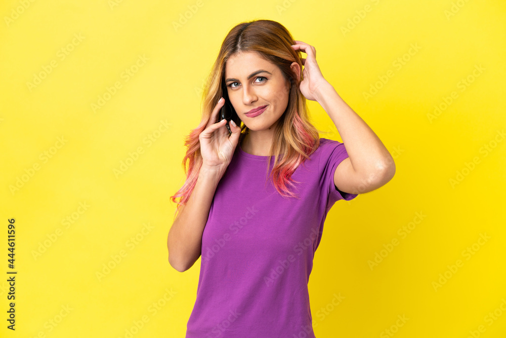 Young woman using mobile phone over isolated yellow background having doubts Young woman using mobile phone over isolated yellow background having doubts