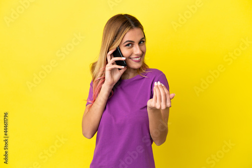 Young woman using mobile phone over isolated yellow background inviting to come with hand. Happy that you came © luismolinero