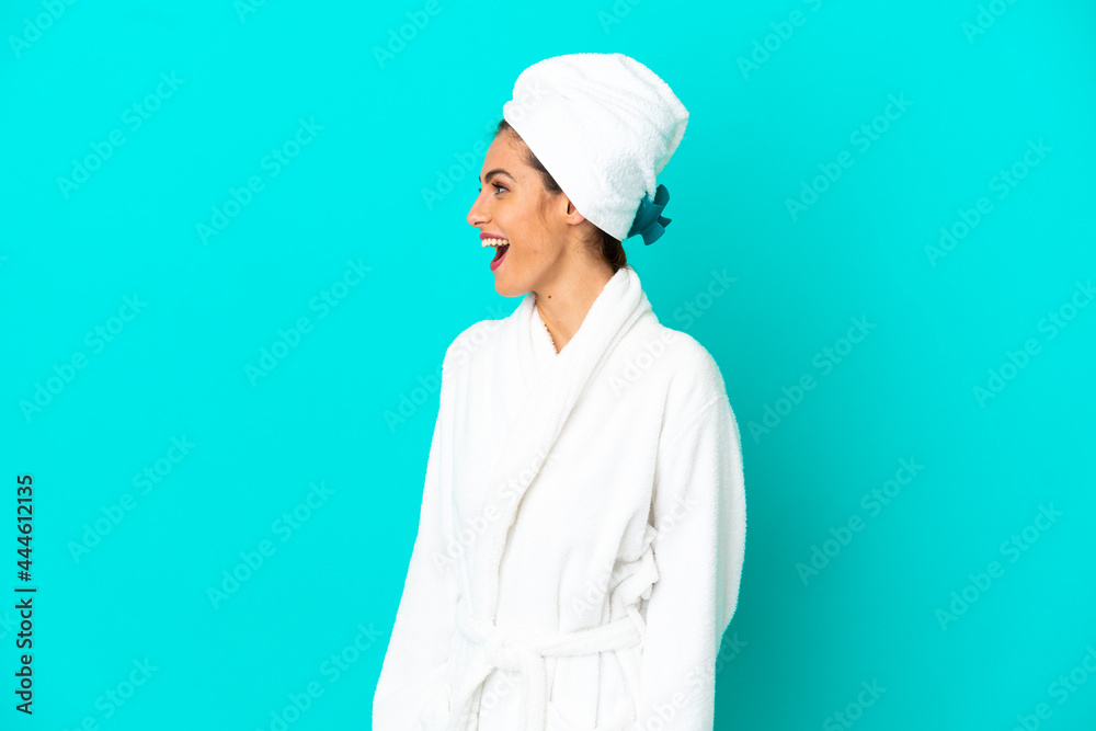 Young woman in a bathrobe over isolated blue background laughing in lateral position Young woman in a bathrobe over isolated blue background laughing in lateral position