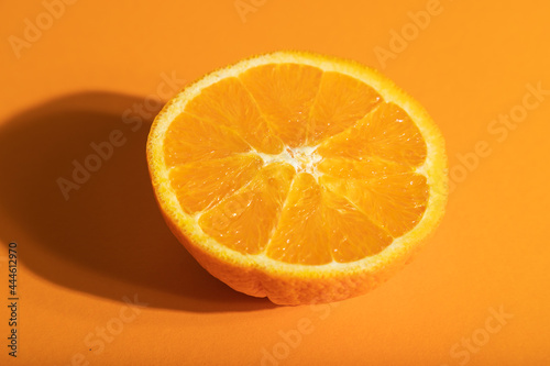 Ripe cut orange on orange pastel background. Side view, close up, hard light.