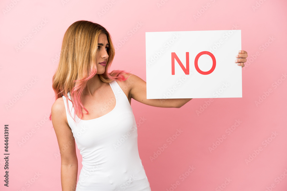 Young woman over isolated pink background holding a placard with text NO Young woman over isolated pink background holding a placard with text NO