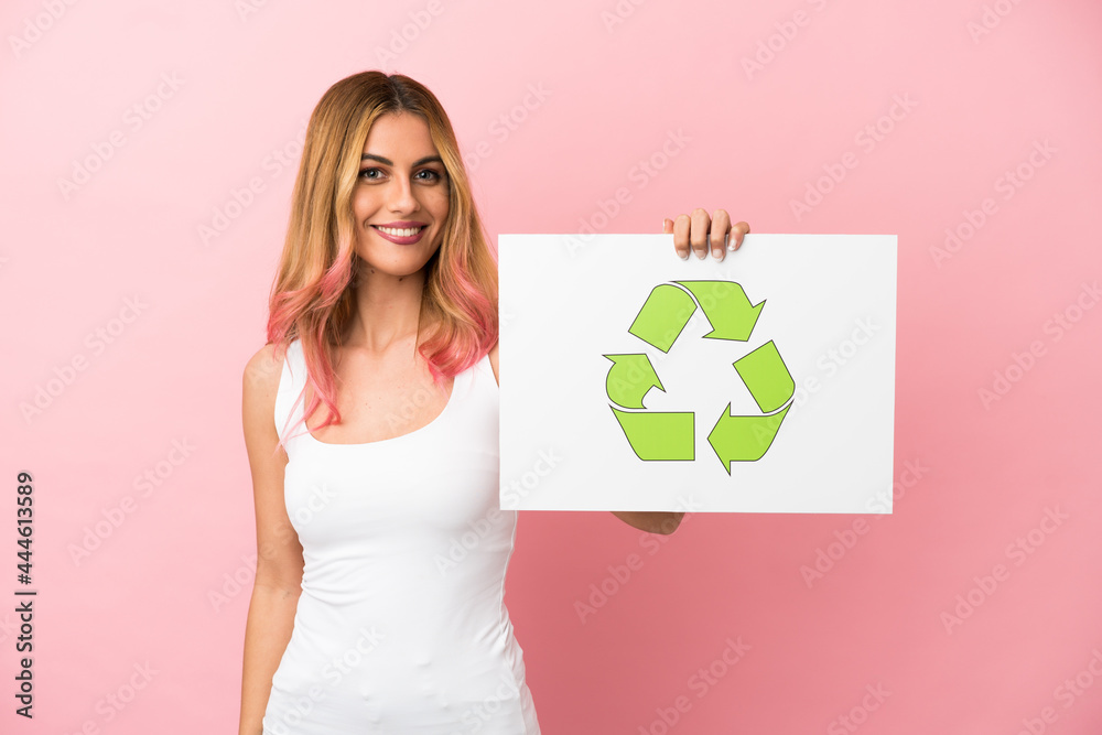 Young woman over isolated pink background holding a placard with recycle icon with happy expression