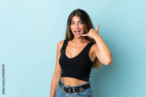 Young caucasian woman isolated on blue background making phone gesture. Call me back sign © luismolinero