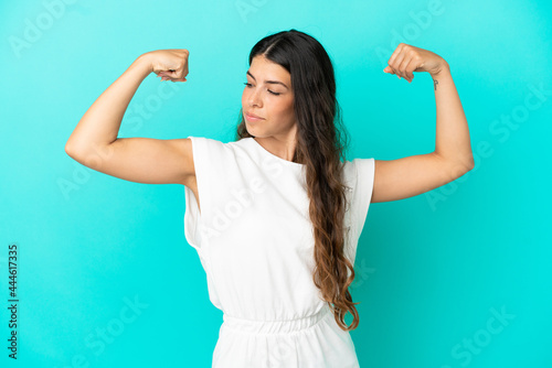 Young caucasian woman isolated on blue background doing strong gesture