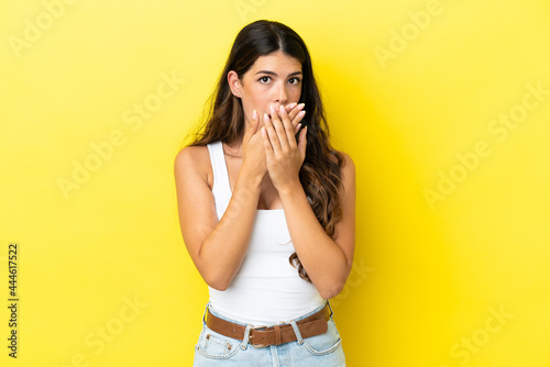 Young caucasian woman isolated on yellow background covering mouth with hands