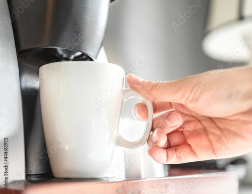 Woman using coffee maker, brewing hot beverage in the morning with blurred background. Automatic coffee machine at snack bar in hotel room. Person making caffeine drink at an office.