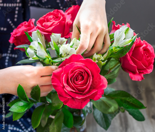 Woman florist hands making mix fresh flowers with green leaves for special anniversary. Closeup bunch of beautiful blossom red roses, selective focus. Specialist concept. Arranging for wedding bouquet