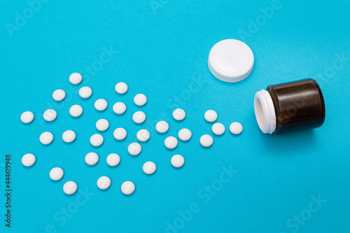Global Pharmaceutical Industry and Medicinal Products - White Pills or Tablets Scattered from the Bottle, Lying on Blue Background