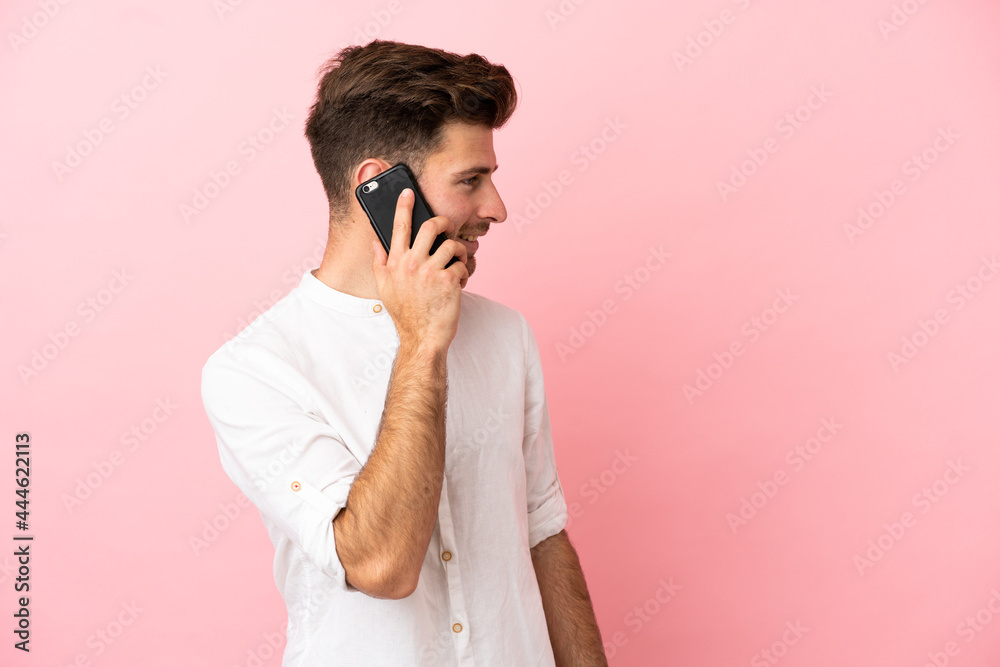 Young caucasian handsome man isolated on pink background keeping a conversation with the mobile phone with someone Young caucasian handsome man isolated on pink background keeping a conversation with the mobile phone with someone
