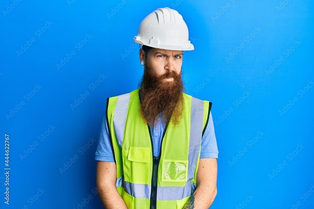 Redhead man with long beard wearing safety helmet and reflective jacket skeptic and nervous, frowning upset because of problem. negative person.
