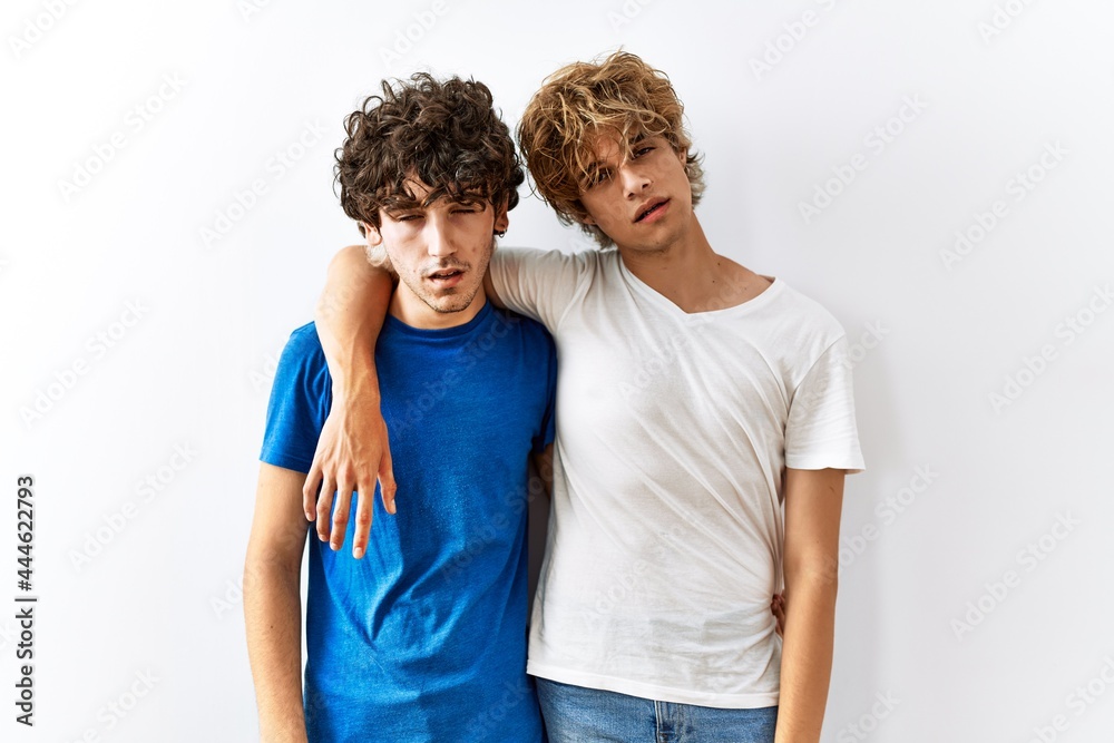 Young gay couple standing together over isolated background looking sleepy and tired, exhausted for fatigue and hangover, lazy eyes in the morning. Young gay couple standing together over isolated background looking sleepy and tired, exhausted for fatigue and hangover, lazy eyes in the morning.