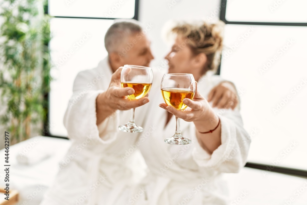 Senior caucasian couple smiling happy toasting with champagne sitting on massage table at beauty center. Senior caucasian couple smiling happy toasting with champagne sitting on massage table at beauty center.
