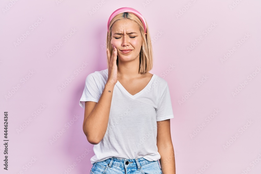 Beautiful blonde woman wearing casual white t shirt touching mouth with hand with painful expression because of toothache or dental illness on teeth. dentist Beautiful blonde woman wearing casual white t shirt touching mouth with hand with painful expression because of toothache or dental illness on teeth. dentist