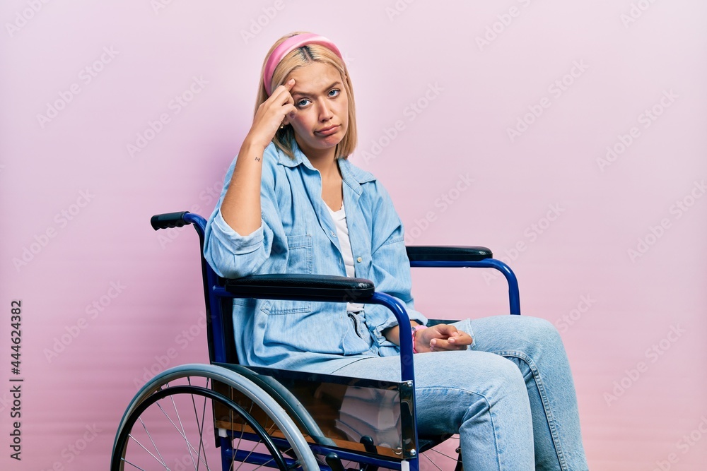 Beautiful blonde woman sitting on wheelchair worried and stressed about a problem with hand on forehead, nervous and anxious for crisis Beautiful blonde woman sitting on wheelchair worried and stressed about a problem with hand on forehead, nervous and anxious for crisis