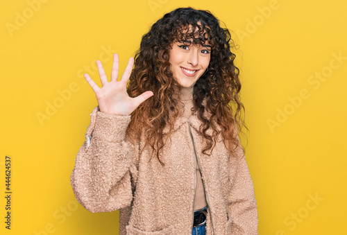 Young hispanic girl wearing winter clothes showing and pointing up with fingers number five while smiling confident and happy.