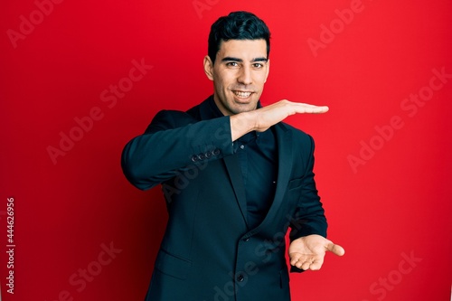 Handsome hispanic man wearing business clothes gesturing with hands showing big and large size sign, measure symbol. smiling looking at the camera. measuring concept.