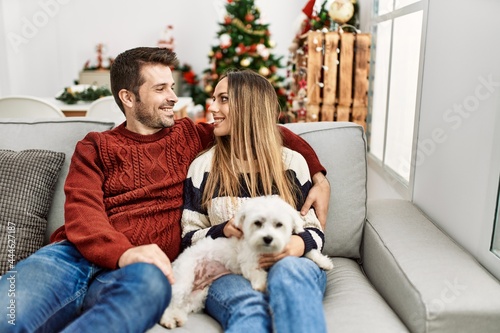 Young hispanic couple smiling happy sitting on the sofa with dog at home.