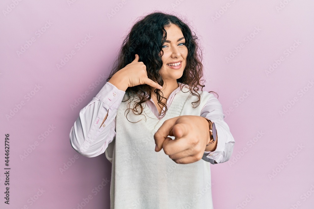 Young brunette woman with curly hair wearing casual clothes smiling doing talking on the telephone gesture and pointing to you. call me.