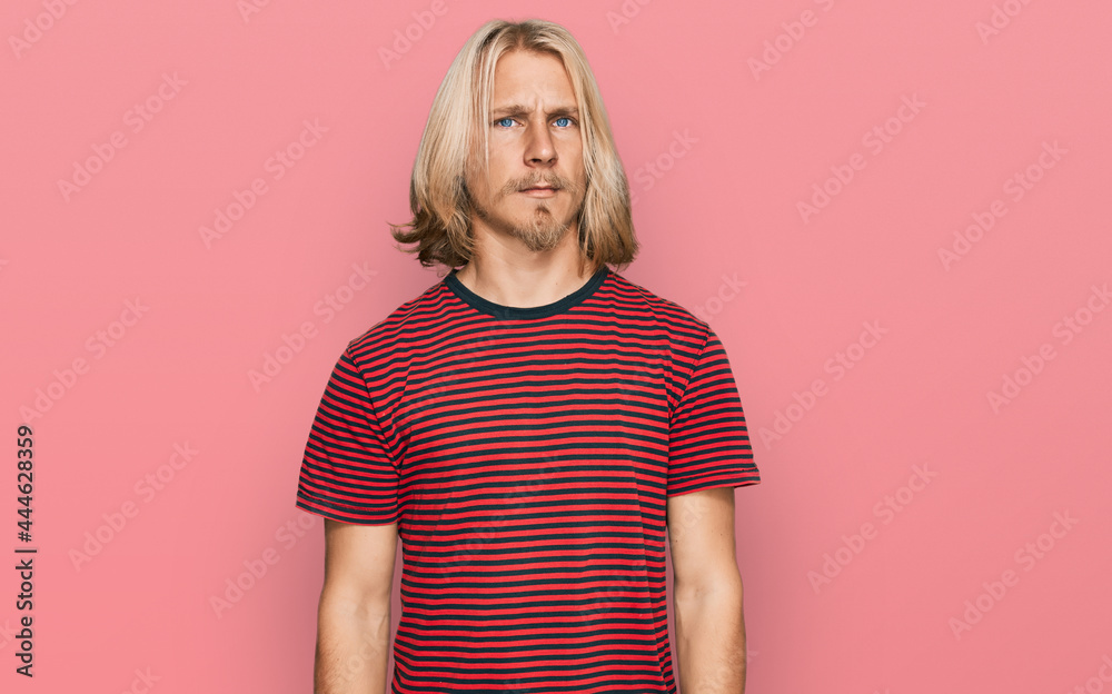 Caucasian man with blond long hair wearing casual striped t shirt skeptic and nervous, frowning upset because of problem. negative person. Caucasian man with blond long hair wearing casual striped t shirt skeptic and nervous, frowning upset because of problem. negative person.