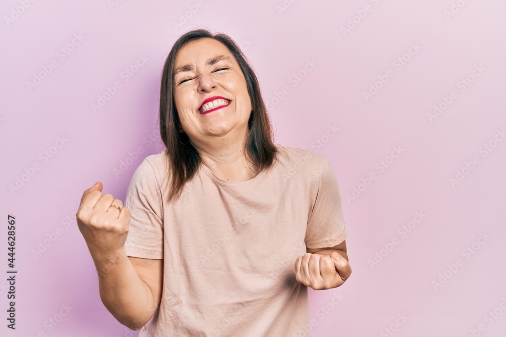 Middle age hispanic woman wearing casual clothes very happy and excited doing winner gesture with arms raised, smiling and screaming for success. celebration concept. Middle age hispanic woman wearing casual clothes very happy and excited doing winner gesture with arms raised, smiling and screaming for success. celebration concept.