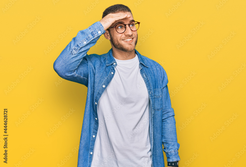 Young caucasian man wearing casual clothes very happy and smiling looking far away with hand over head. searching concept. Young caucasian man wearing casual clothes very happy and smiling looking far away with hand over head. searching concept.