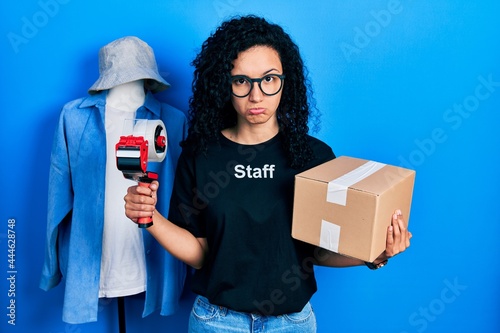 Young hispanic woman with curly hair wearing staff t shirt holding cardboard box depressed and worry for distress, crying angry and afraid. sad expression. photo