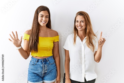 Mother and daughter together standing together over isolated background showing and pointing up with fingers number six while smiling confident and happy.