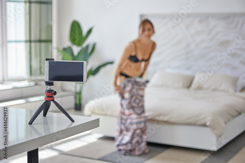 Принти на полотні Young woman undresses in front of smartphone camera, defocused image, selective focus