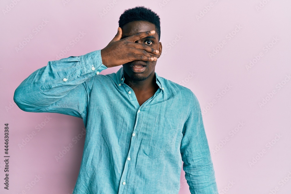 Handsome black man wearing casual clothes peeking in shock covering face and eyes with hand, looking through fingers with embarrassed expression. Handsome black man wearing casual clothes peeking in shock covering face and eyes with hand, looking through fingers with embarrassed expression.